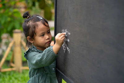 Portrait of cute girl writing alphabet on blackboard