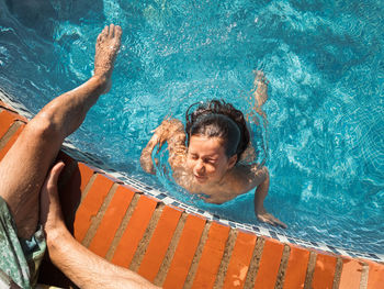 From above anonymous adult man lifeguard cropped leg watching little girl swimming in clean water of pool on resort