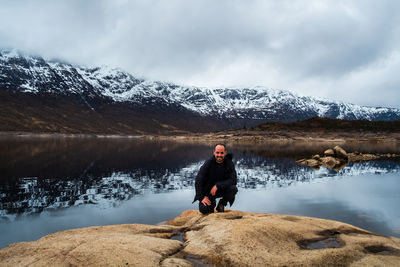 Full length of man standing on rock by lake against sky