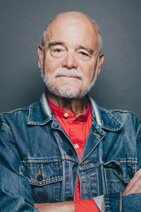 Portrait of confident senior man with arms crossed against gray background