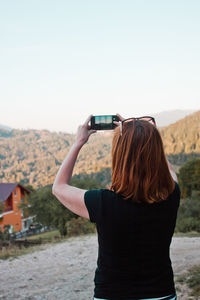 Rear view of woman photographing mountains from mobile phone