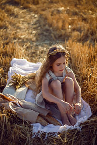 Girl child sitting on a mown wheat field at sunset with bread