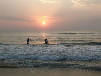 Silhouette people on beach against sky during sunset