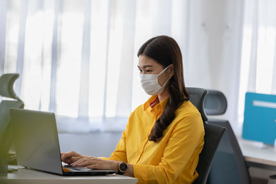 Cheerful businesswoman wearing mask using laptop in office