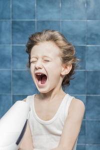 Cute boy with mouth open holding dryer against wall