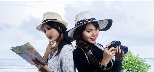 Woman reading map while friend using camera against sky