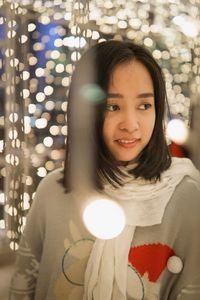 Portrait of young woman standing against illuminated lights