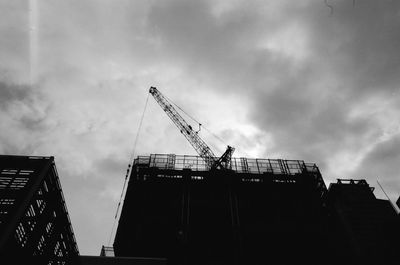 Low angle view of crane against cloudy sky