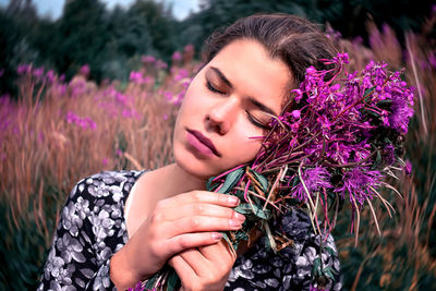 Beautiful woman holding purple flowers against field