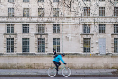 Blurred motion of man riding bicycle against building