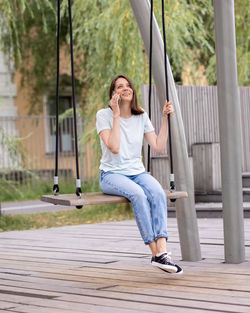 A young and confident woman blogger or freelancer rides a swing and talks on the phone