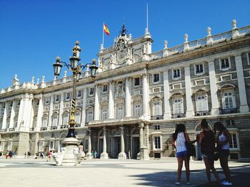 People in front of palacio real de madrid against clear blue sky in city