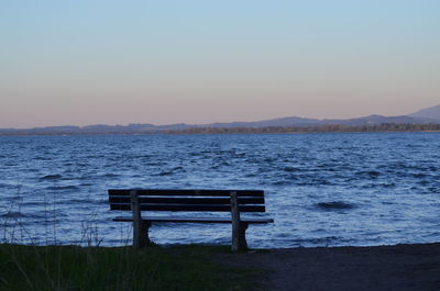 Empty bench by sea against sky during sunset