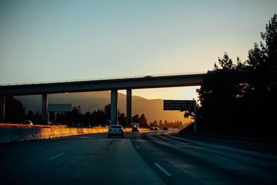 Cars on highway below bridge against sky