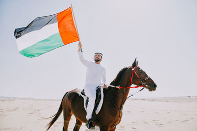 Man riding umbrellas on beach against sky