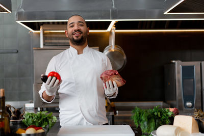 Portrait of chef holding meat and vegetable at kitchen