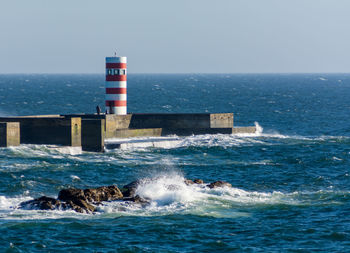 Lighthouse by sea against clear sky