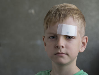 Close-up portrait of boy with bandage on forehead against gray background