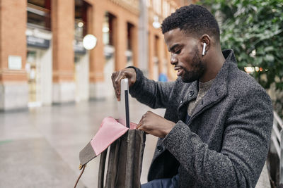 Young man putting laptop in bag against plants