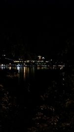 Illuminated buildings by sea against sky at night