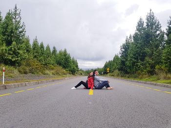 Couple sitting on road against sky