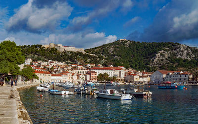 Sailboats moored in harbor by buildings in city against sky