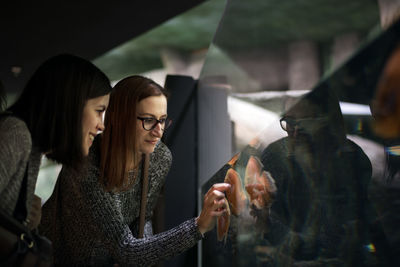 Female friends looking at fish swimming at aquarium