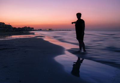 Silhouette man standing on beach against sky during sunset