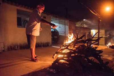 Man standing by illuminated fire at night