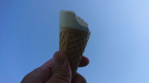 Hand holding ice cream against blue sky