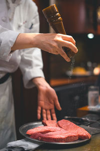 Midsection of chef seasoning salt on meat