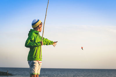 Boy fishing in sea against sky