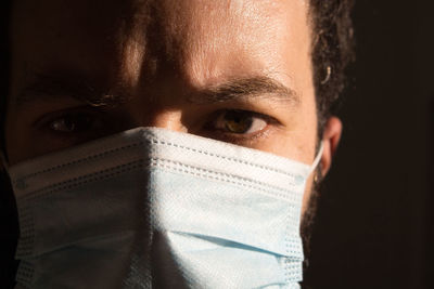 Close-up portrait of man wearing flu mask against black background