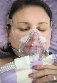 Close-up of patient wearing oxygen mask while lying on bed in hospital