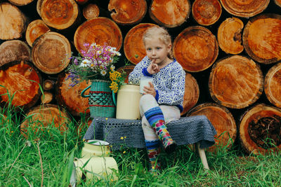 Rustic style, a girl in casual clothes sits on a bench against the background of a woodpile