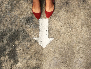 Low section of woman standing in front of arrow sign on road