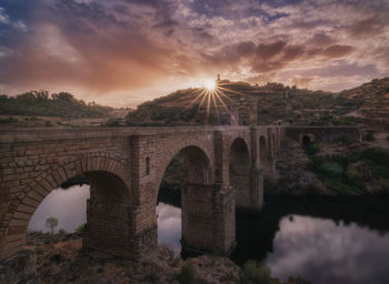 Arch bridge over river against sky during sunset