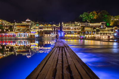 River by illuminated buildings against sky at night