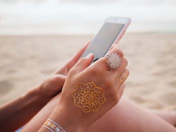 Close-up of woman holding mobile phone at beach