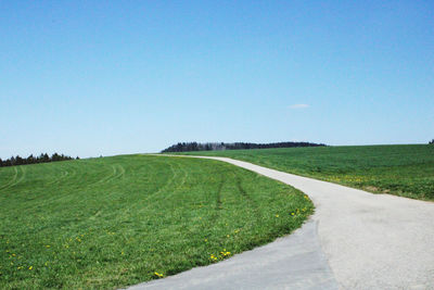 Scenic view of road amidst field against clear blue sky