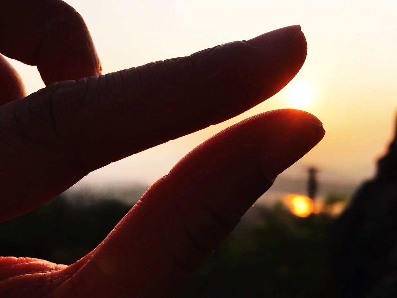 CLOSE-UP OF HAND HOLDING SUN DURING SUNSET