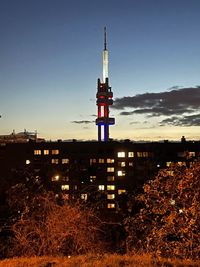 Tower amidst buildings against sky at sunset