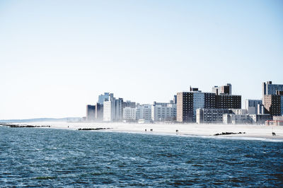 Sea by buildings against clear sky