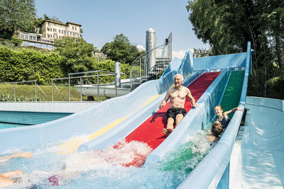 Grandfather and grandchildren enjoying water slide in swimming pool