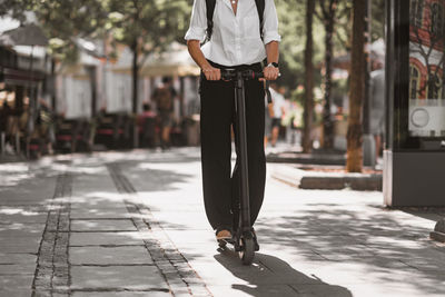 Low section of man standing over push scooter on footpath