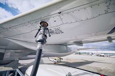 Airplane refueling at airport runway against sky