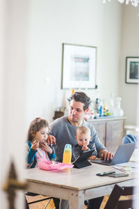 Father sitting with son while looking at girl watching movie on digital tablet