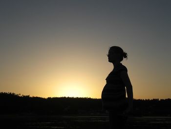 Side view of pregnant woman standing against sky during sunset