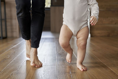 Low section of woman walking with baby on hardwood floor