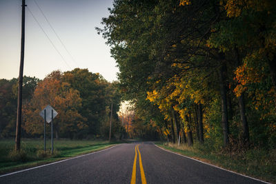 Country road amidst trees against sky during autumn